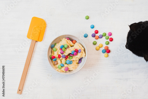 Black cat trying to steal from bowl of cookie dough and Spatula on white wooden background