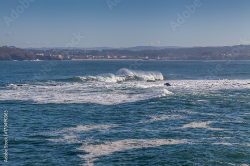 view from coastal coruna in Spain onto blue waters of Atlantic Ocean with white waves and houses © osnuya