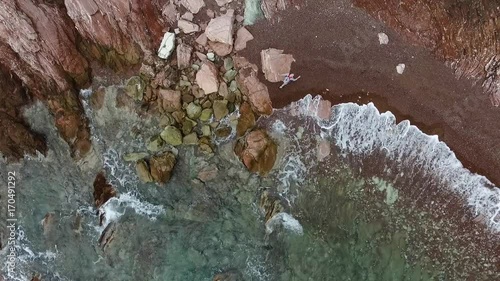 Stone beach and green trees. Footage. Woman on the shore the rocky shore of the sea, top view photo