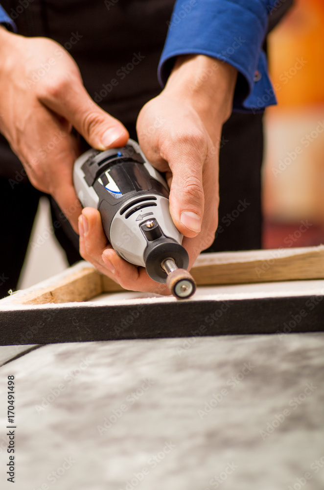 Closeup of a hardworker man using a polisher in a wooden frame, on a gray table in a blurred background