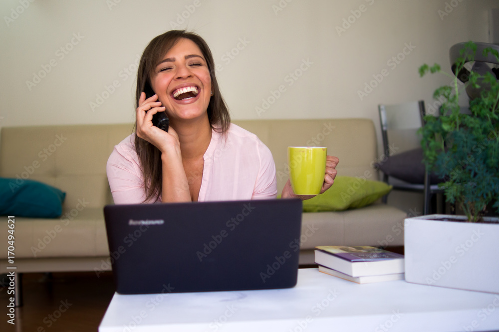 Mujer joven y bella hablando por teléfono frente al computador en la comodidad de su hogar Mujer joven y bella hablando por teléfono frente al computador en la comodidad de su hogar