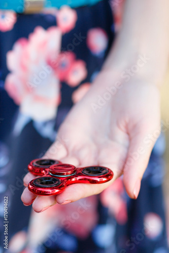 A girl is holding a popular toy fidget spinner in her hands. Stress relief. Anti stress and relaxation fidgets, spinner for tired people. Girl playing with a red fidget spinner.