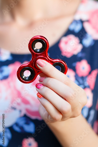 A girl is holding a popular toy fidget spinner in her hands. Stress relief. Anti stress and relaxation fidgets, spinner for tired people. Girl playing with a red fidget spinner.