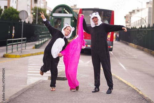 Close up of a happy group of friends wearing different costumes, one woman wearing a pink unicorn costume, other woman a panda costume and the man wearing a cat costume, in the city of Quito