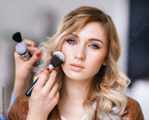 Process of applying makeup on the girl's face close-up. Model is waiting for make-up artist to finish work.