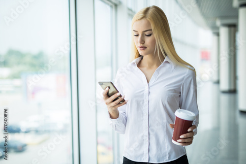 Free Download Busy businesswoman use the phone with cup of coffee in other hand near big panoramic window in the office - GFXLoad