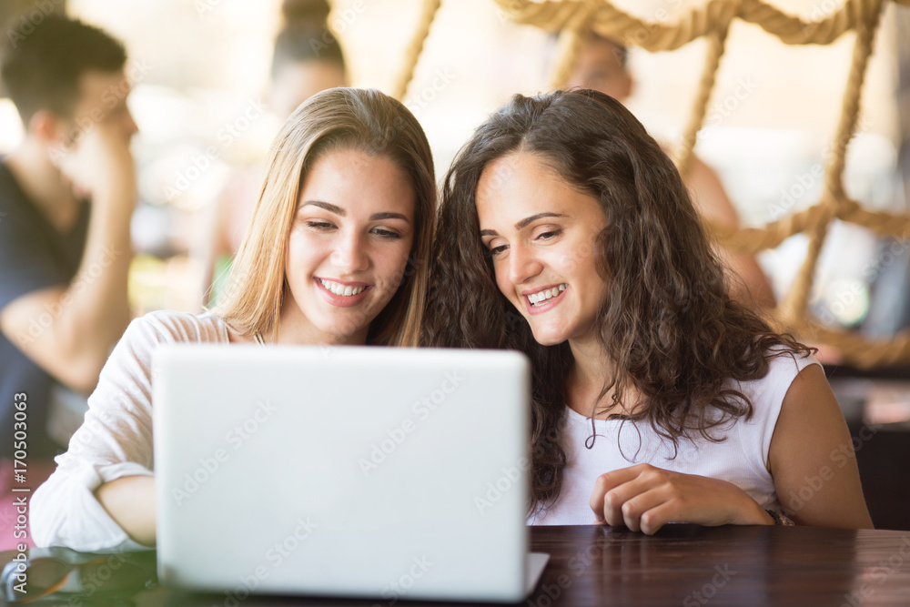 Two young women looking at laptop and smiling Two young women looking at laptop and smiling