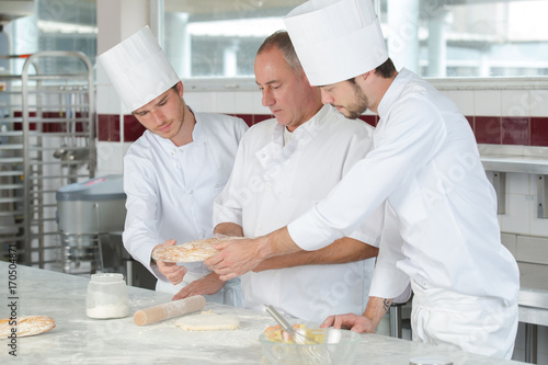 chef with 2 young cooks in kitchen preparing dish