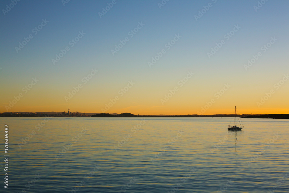 Golden and orange light closes the day over Auckland and the serene Waitemata Habour, New Zealand
