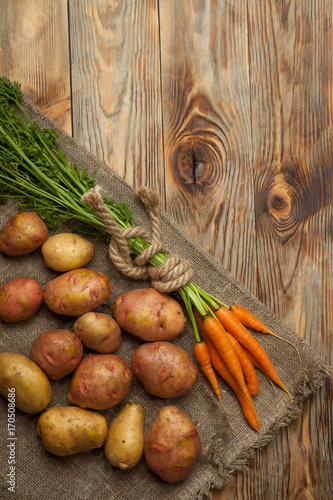 Raw potatoes and carrots on a wooden background
