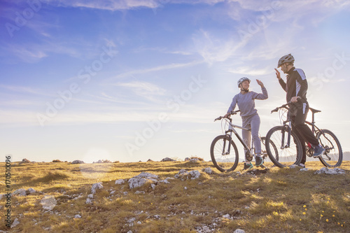 happy couple goes on a mountain asphalt road in the woods on bikes with helmets giving each other a high five