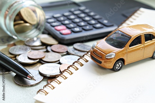 Business, finance, saving money, banking or car loan concept : Miniature car model, calculator, coins scattered from glass jar, notebook paper and pen on office desk table