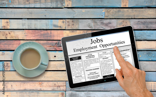 Online job hunting Hand with computer tablet reading employment ads on table with coffee
