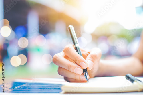 Woman's hand writing on a notepad with a pen on a wooden desk.