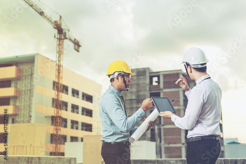 smiling young architect or engineering builder in hard hat with tablet over group of builders at construction site, architect watching some a construction, business, building, industry, people concept