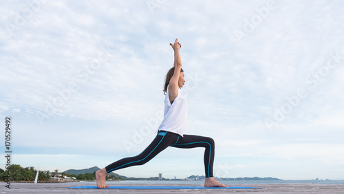 Middle age women in a yoga posture, hands up in the air along the beach