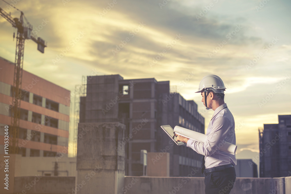 Smiling young architect or engineering builder in hard hat with tablet over group of builders at construction site, architect watching some a construction, business, building, industry, people concept Smiling young architect or engineering builder in hard hat with tablet over group of builders at construction site, architect watching some a construction, business, building, industry, people concept