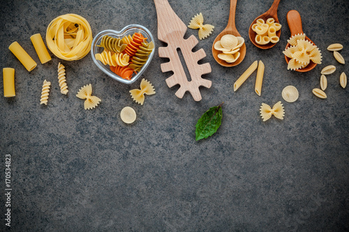 Italian foods concept and menu design. Various kind of Pasta Farfalle, Pasta A Riso, Orecchiette Pugliesi, Gnocco Sardo and Farfalle in wooden spoons setup on stone background with flat lay.