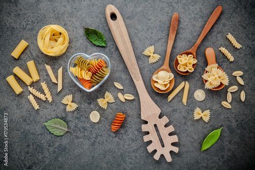 Italian foods concept and menu design. Various kind of Pasta Farfalle, Pasta A Riso, Orecchiette Pugliesi, Gnocco Sardo and Farfalle in wooden spoons setup on stone background with flat lay.