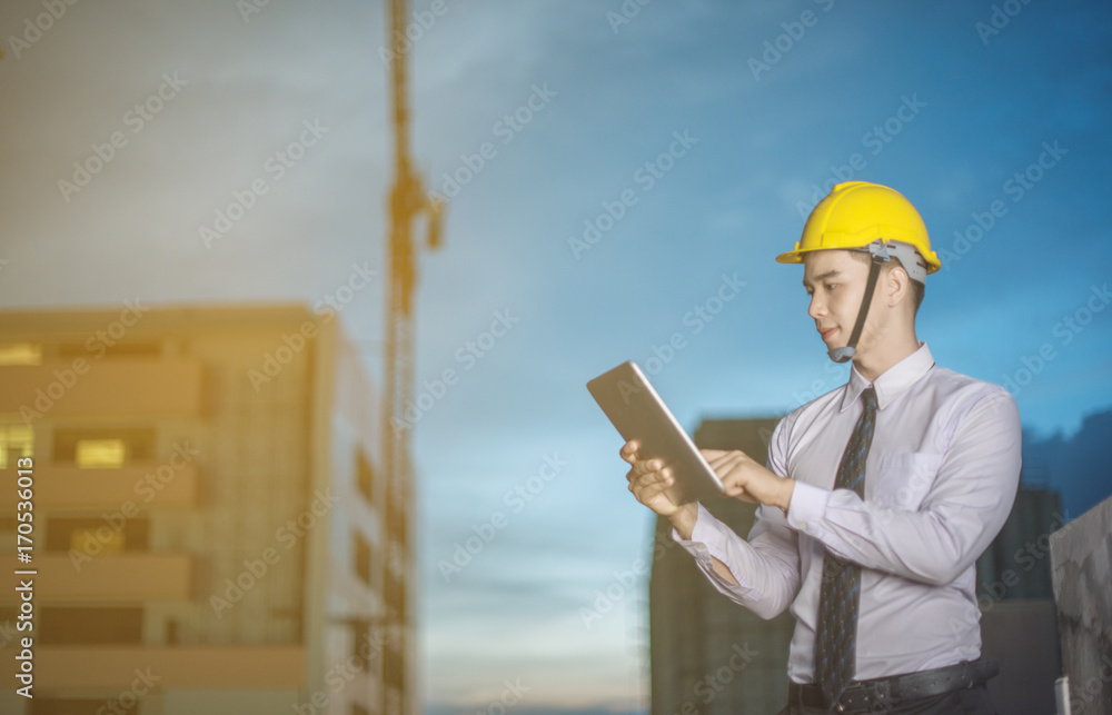 Smiling young architect or engineering builder in hard hat with tablet over group of builders at construction site, architect watching some a construction, business, building, industry, people concept Smiling young architect or engineering builder in hard hat with tablet over group of builders at construction site, architect watching some a construction, business, building, industry, people concept