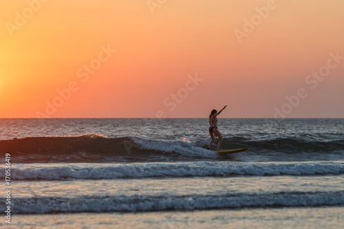 Surfing at Sunset. Beautiful Young Woman Riding Wave at Sunset. Outdoor Active Lifestyle.