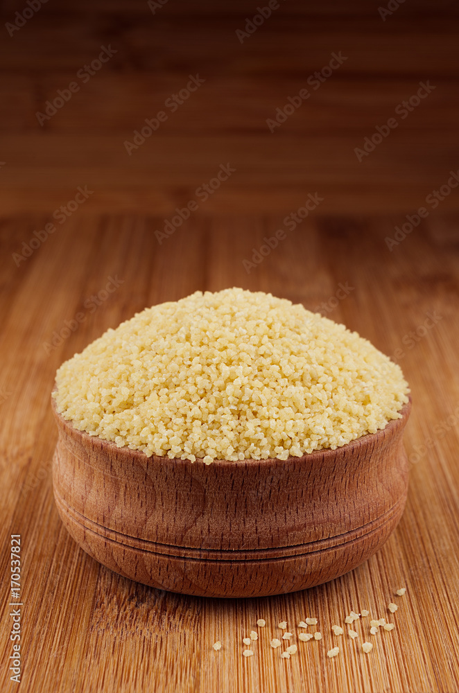 Couscous in wooden bowl on brown bamboo board, closeup. Rustic style, healthy dietary groats background. Couscous in wooden bowl on brown bamboo board, closeup. Rustic style, healthy dietary groats background.