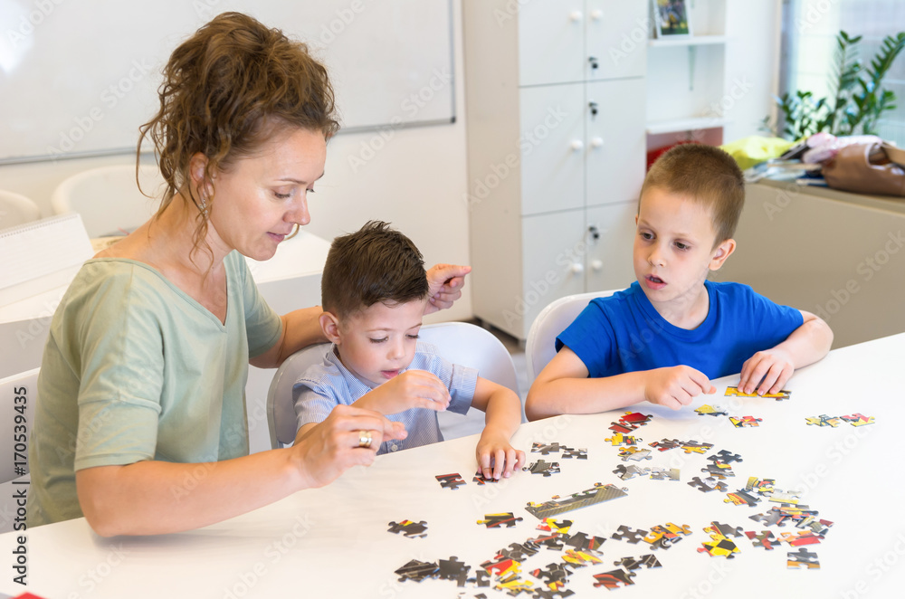 teacher woman and two preschooler boy playing with puzzle game in the classroom teacher woman and two preschooler boy playing with puzzle game in the classroom