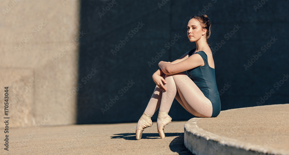 Fototapeta premium Female ballet dancer sitting gracefully while resting her toes o