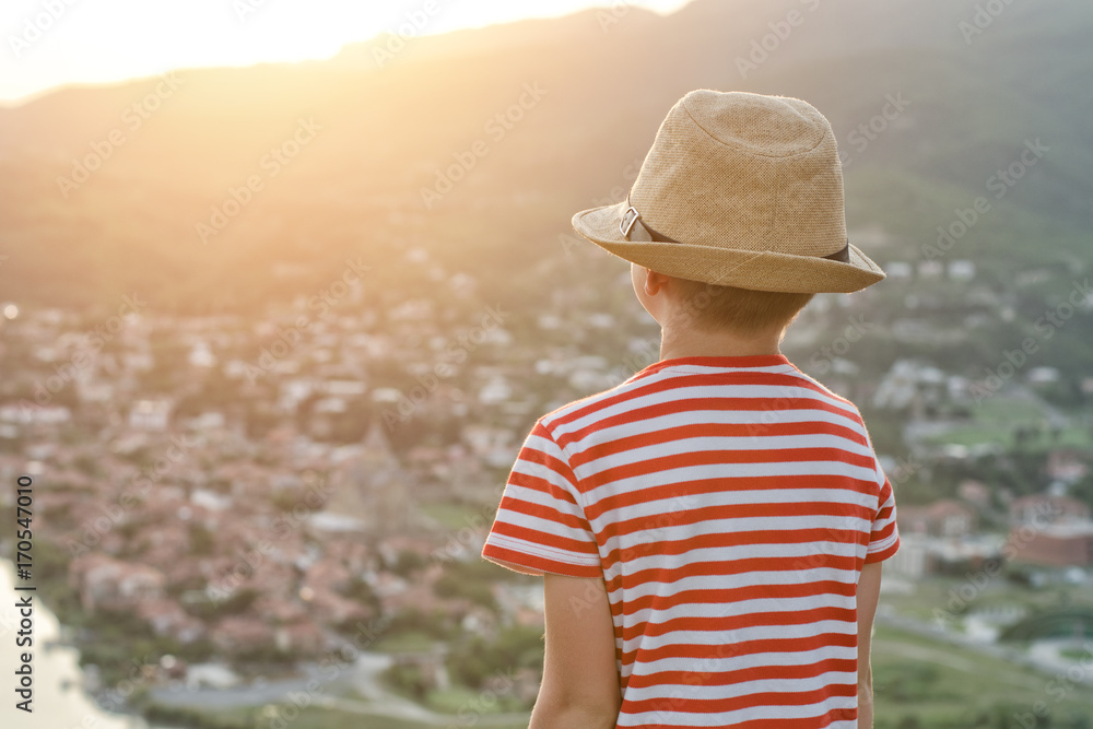 Boy in hat looking at the city from a height. Rear view, evening time