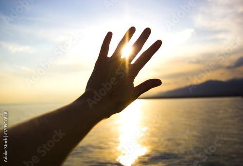 sun shining through the fingers of the hand on the sea background