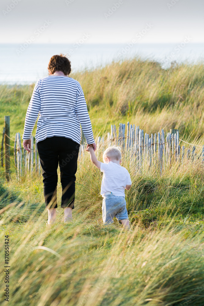 Child and grandmother walking together outside at the beach