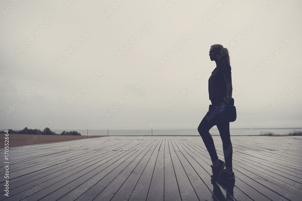 Fototapeta premium Silhouette of a young boxer woman standing on a wooden sports-ground