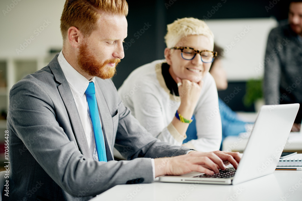 Fototapeta premium Businessman using laptop and sitting in modern office while colleague helping him
