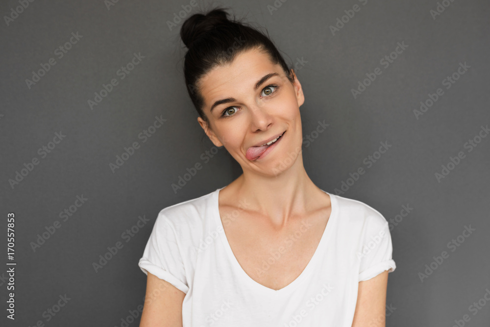 Funny young brunette teenage female with hair knot sticking out her tongue having crazy positive look isolated over gray background. Student girl happy to finish her studying successfully exams. Funny young brunette teenage female with hair knot sticking out her tongue having crazy positive look isolated over gray background. Student girl happy to finish her studying successfully exams.