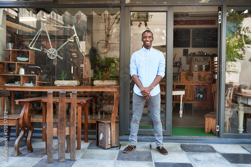 Smiling African entrepreneur standing welcomingly in front of his cafe © mavoimages