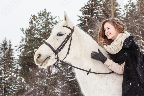 Nice girl and white horse outdoor in snowfall in a winter