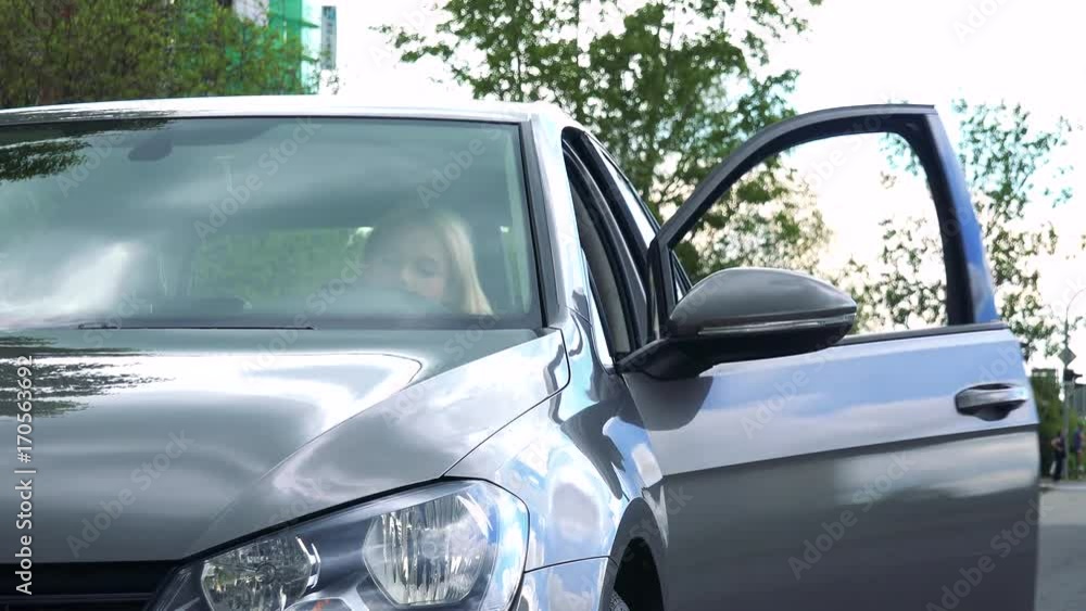 young attractive blond woman gets in the car on the street with trees young attractive blond woman gets in the car on the street with trees