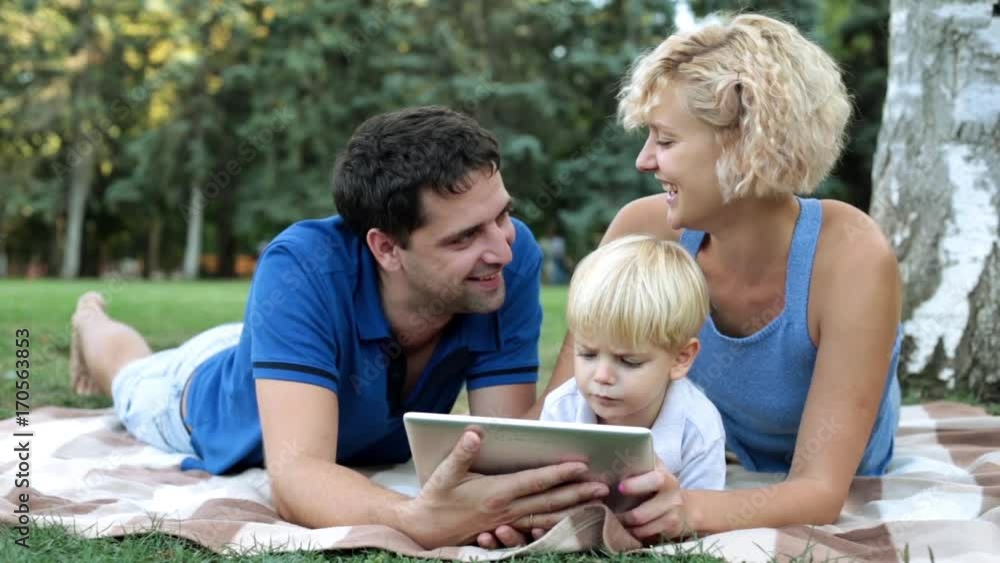 Happy family with baby enjoying a tablet computer in the park. Family and modern technology. Happy family with baby enjoying a tablet computer in the park. Family and modern technology.