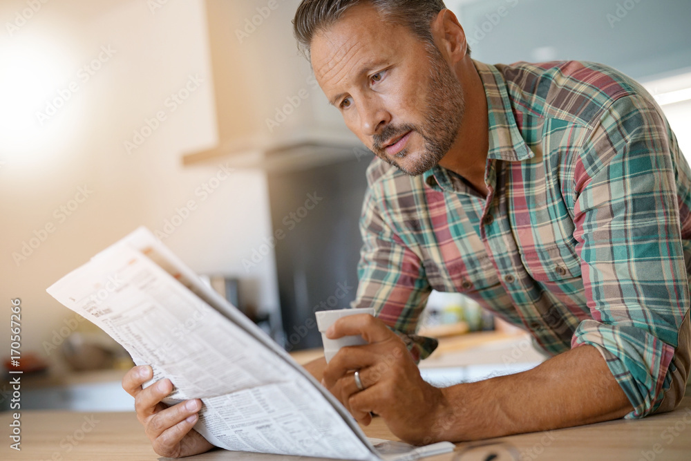 Smiling mature man drinking coffee and reading newspaper Smiling mature man drinking coffee and reading newspaper