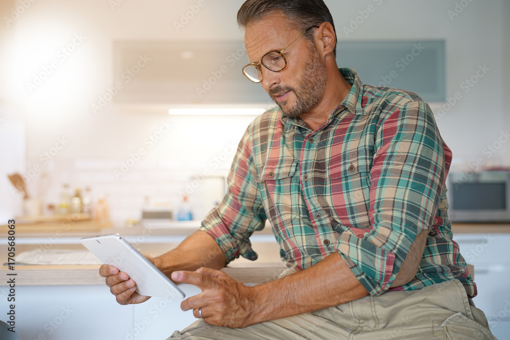 Mature man with eyeglasses using digital tablet at home Mature man with eyeglasses using digital tablet at home