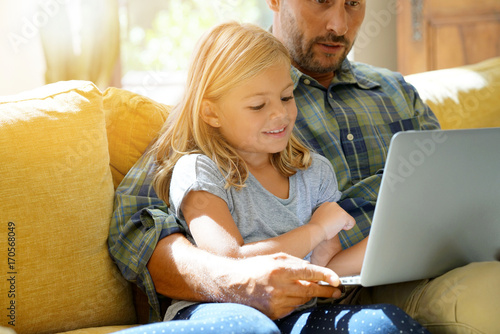 Daddy with little girl using laptop, sitting on couch photo