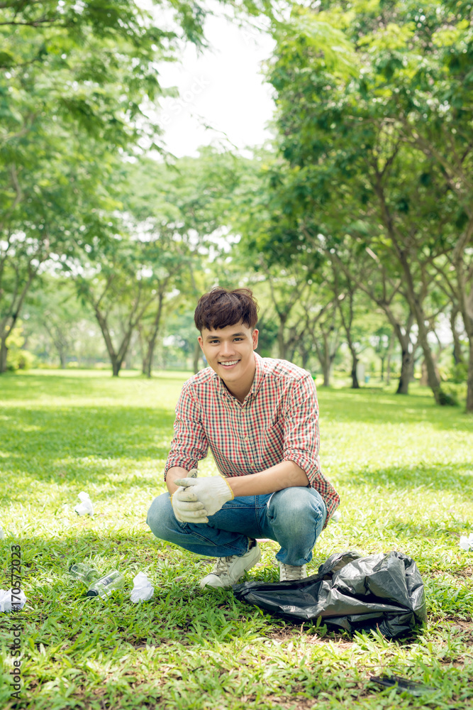 Young man crouching to waste and picking it up in bin bag Young man crouching to waste and picking it up in bin bag