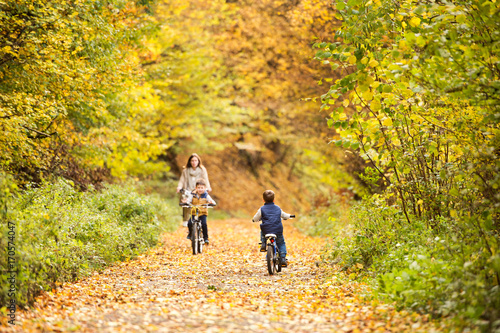 Mother with little sons cycling in autumn park.