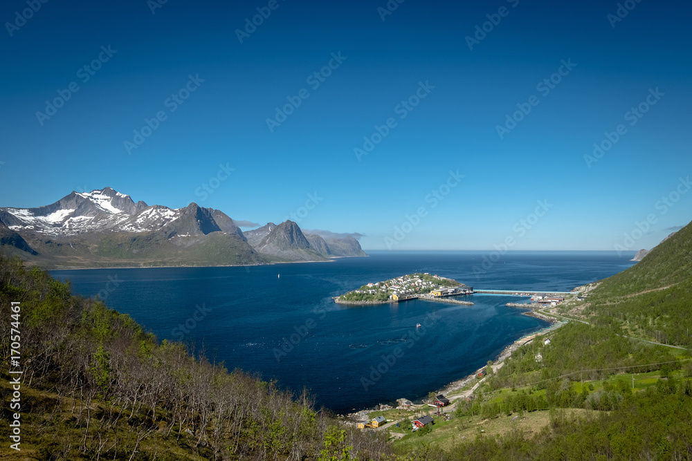 Scenic view of remote town of Husoy, Senja Norway with snowy peaks in distance.