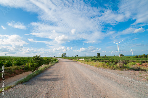 Dirt road with wind mill turbine in blue sky day.