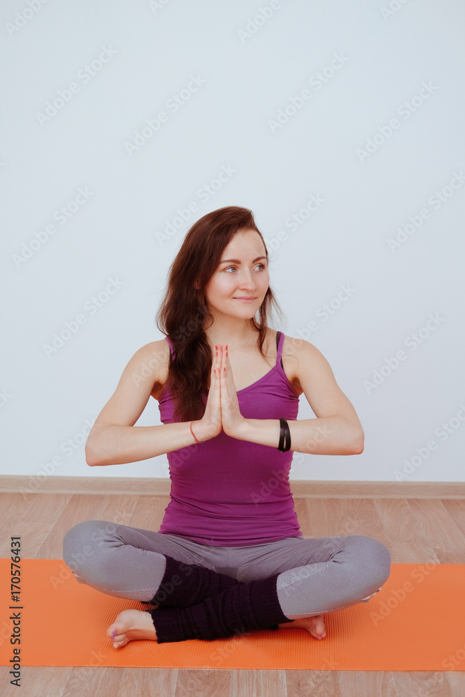 Healthy lifestyle. The girl is practicing meditation on the gym mat in yoga class. Relaxation and Stretching. Young slim sporty girl holds her hands in Namaste posture! Woman do yoga lotus position. Healthy lifestyle. The girl is practicing meditation on the gym mat in yoga class. Relaxation and Stretching. Young slim sporty girl holds her hands in Namaste posture! Woman do yoga lotus position.