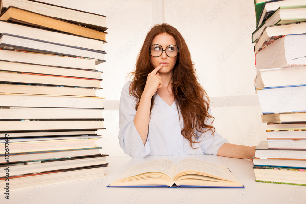 attractive young woman studies wtih hugr book piles on her desk attractive young woman studies wtih hugr book piles on her desk