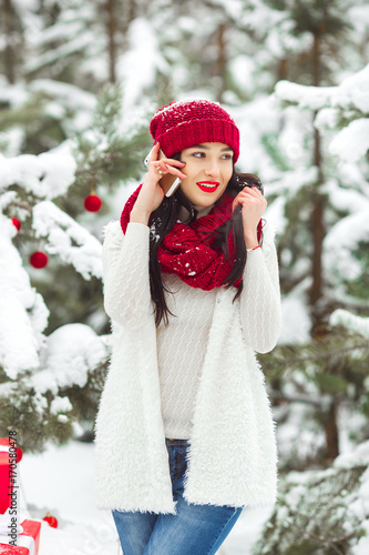 Pretty woman talking on a mobile phone and holding christmas presents. Cheerful young girl smiling a side of camera outdoors