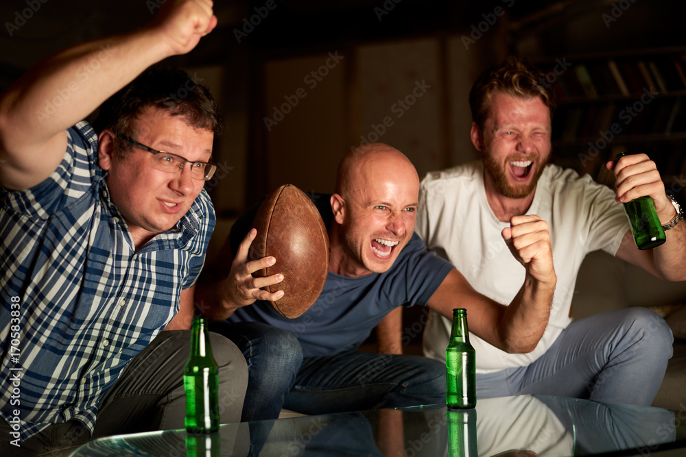 Fototapeta premium Three friends watching american football game on television