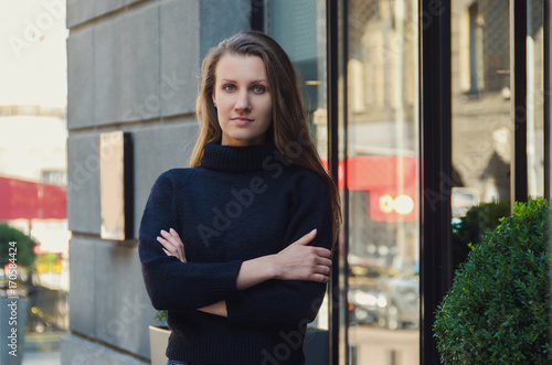 Stylish, slender, confident woman stands on the city street in black sweater,